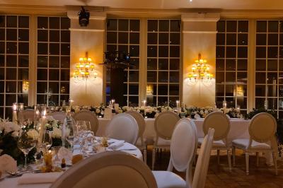 Salle de réception élégante avec tables dressées, chaises blanches et décorations florales sous un éclairage chaleureux.