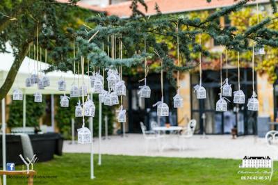 Allée gravillonnée bordée de lanternes blanches menant à un jardin arboré, vue depuis un portail en fer forgé.
