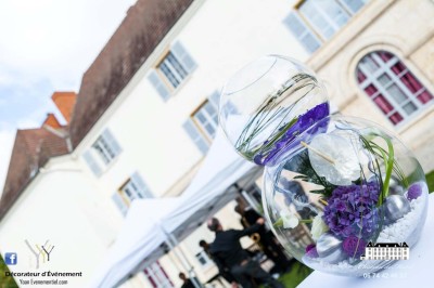 Allée gravillonnée bordée de lanternes blanches menant à un jardin arboré, vue depuis un portail en fer forgé.