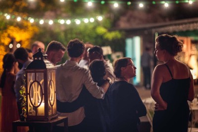Allée gravillonnée bordée de lanternes blanches menant à un jardin arboré, vue depuis un portail en fer forgé.