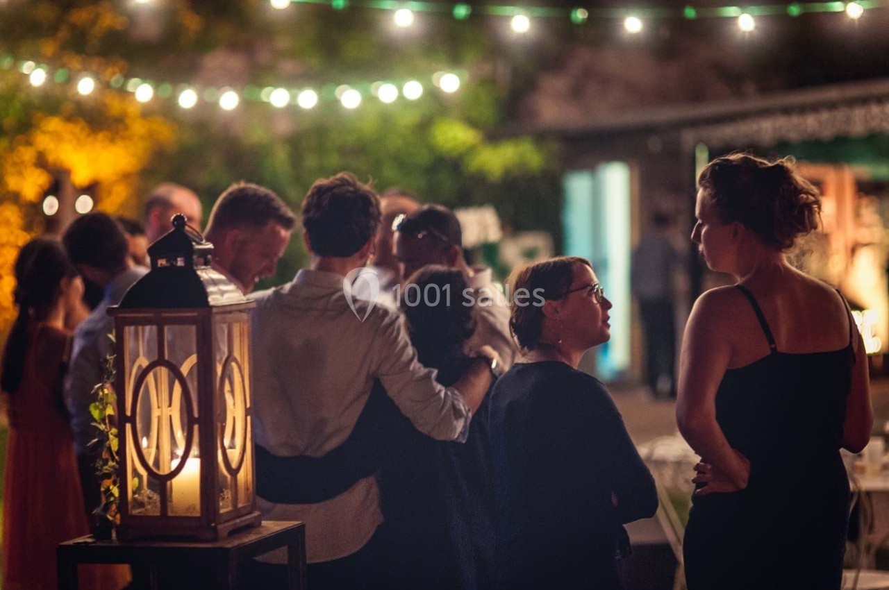 Groupe de personnes discutant dans un jardin éclairé par des guirlandes lumineuses, ambiance chaleureuse en soirée.