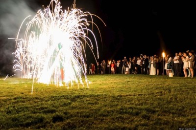 Allée gravillonnée bordée de lanternes blanches menant à un jardin arboré, vue depuis un portail en fer forgé.