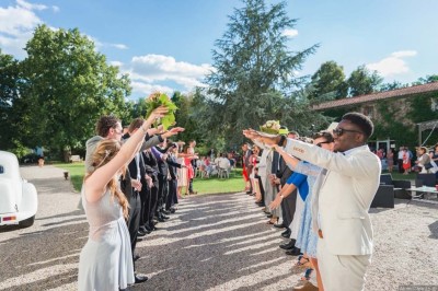 Allée gravillonnée bordée de lanternes blanches menant à un jardin arboré, vue depuis un portail en fer forgé.