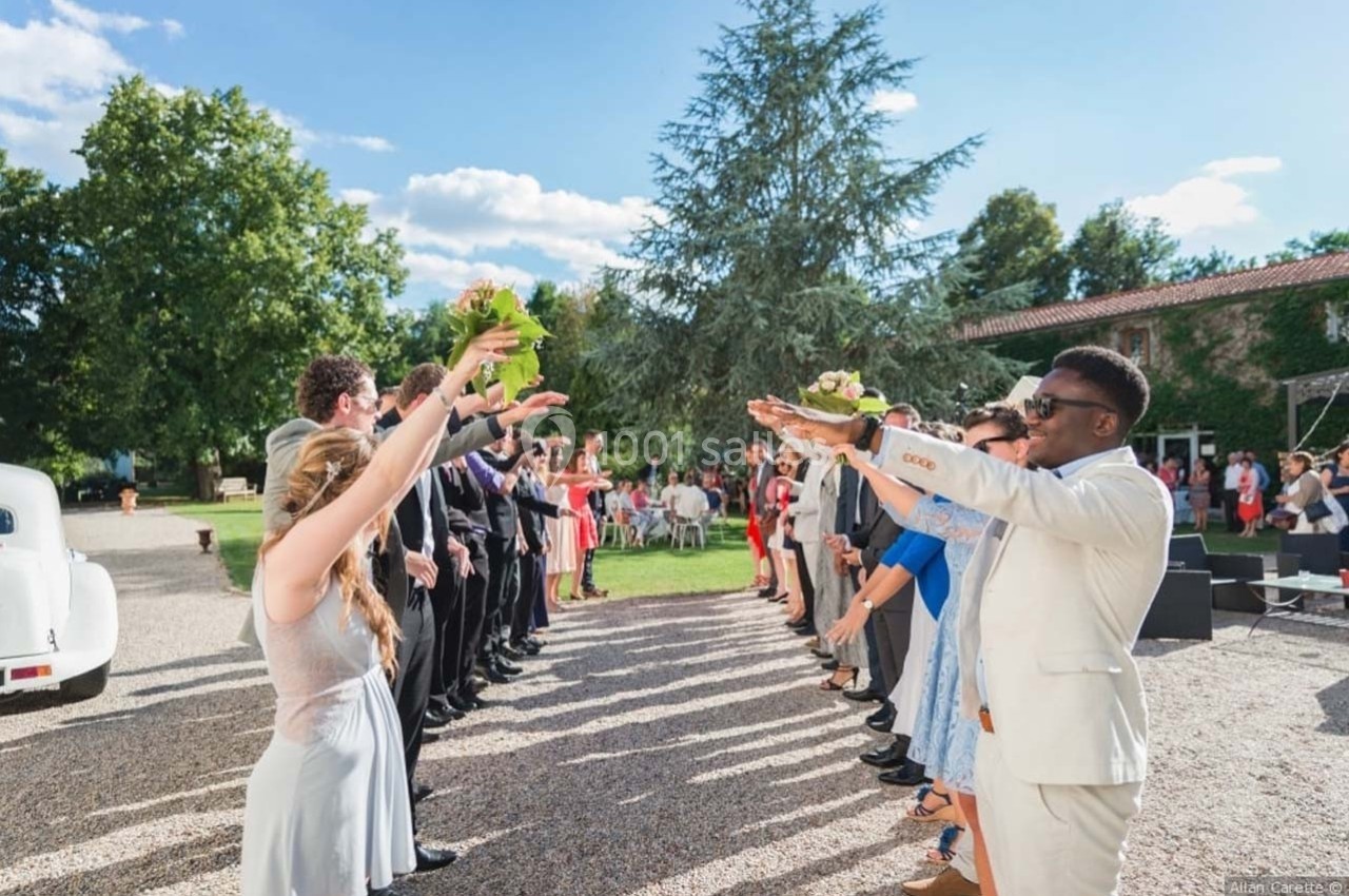 Des invités forment une haie d'honneur en plein air, levant les bras pour accueillir un couple lors d'une cérémonie.