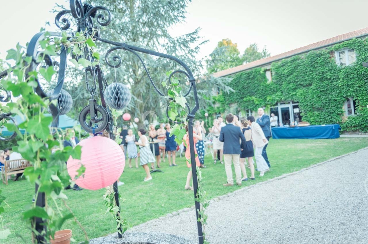 Groupe de personnes discutant dans un jardin, décoré de lanternes et de végétation, près d'un bâtiment couvert de lierre.