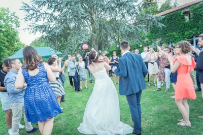 Allée gravillonnée bordée de lanternes blanches menant à un jardin arboré, vue depuis un portail en fer forgé.