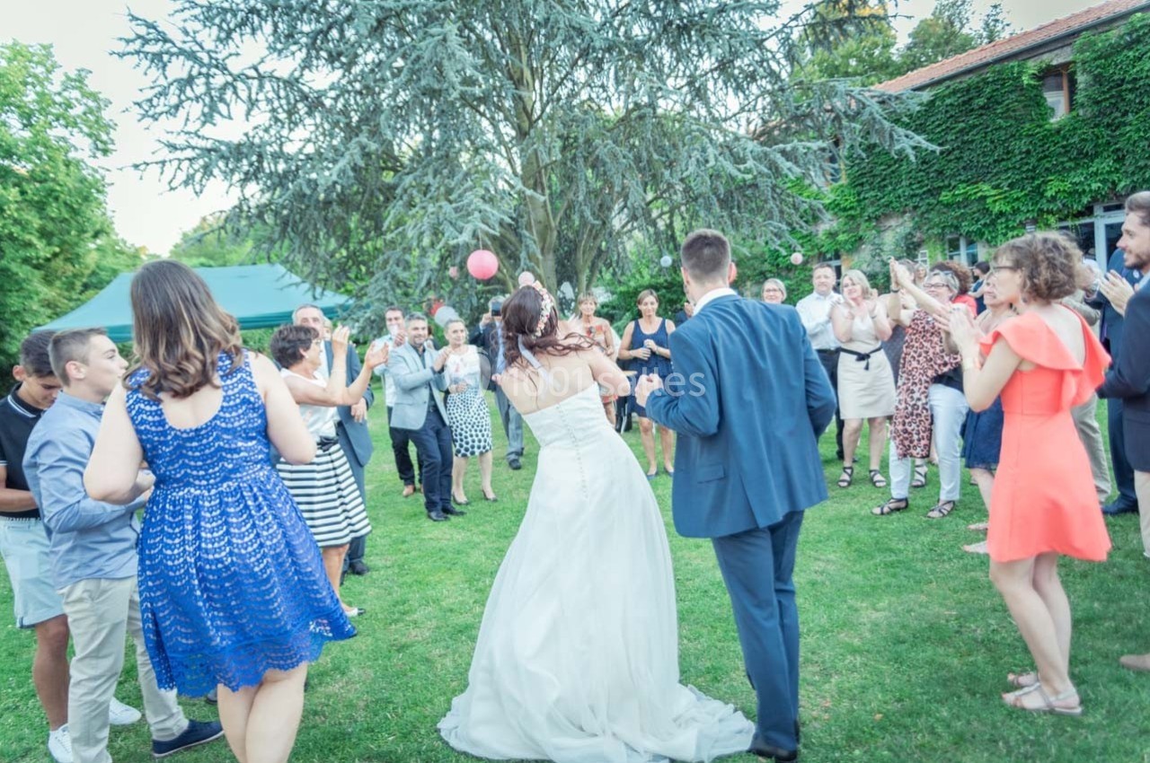 Un couple de mariés danse entouré d'invités applaudissant dans un jardin verdoyant.