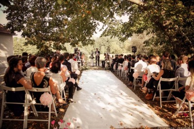 Allée gravillonnée bordée de lanternes blanches menant à un jardin arboré, vue depuis un portail en fer forgé.