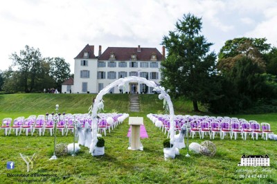 Allée gravillonnée bordée de lanternes blanches menant à un jardin arboré, vue depuis un portail en fer forgé.