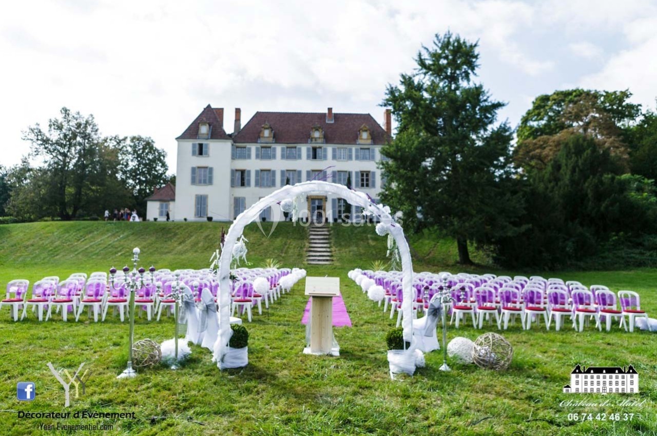Allée centrale décorée pour une cérémonie de mariage en extérieur, devant un grand bâtiment blanc.