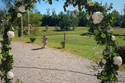 Allée gravillonnée bordée de lanternes blanches menant à un jardin arboré, vue depuis un portail en fer forgé.