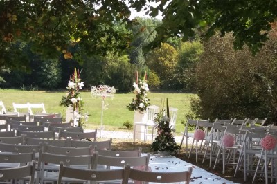 Allée gravillonnée bordée de lanternes blanches menant à un jardin arboré, vue depuis un portail en fer forgé.