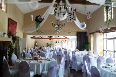 Allée gravillonnée bordée de lanternes blanches menant à un jardin arboré, vue depuis un portail en fer forgé.