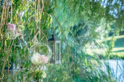 Allée gravillonnée bordée de lanternes blanches menant à un jardin arboré, vue depuis un portail en fer forgé.