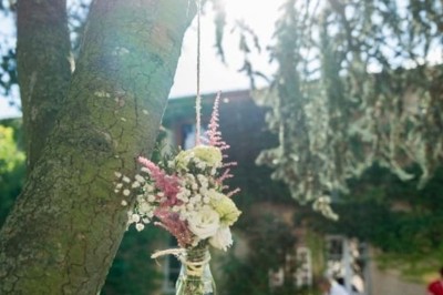 Allée gravillonnée bordée de lanternes blanches menant à un jardin arboré, vue depuis un portail en fer forgé.