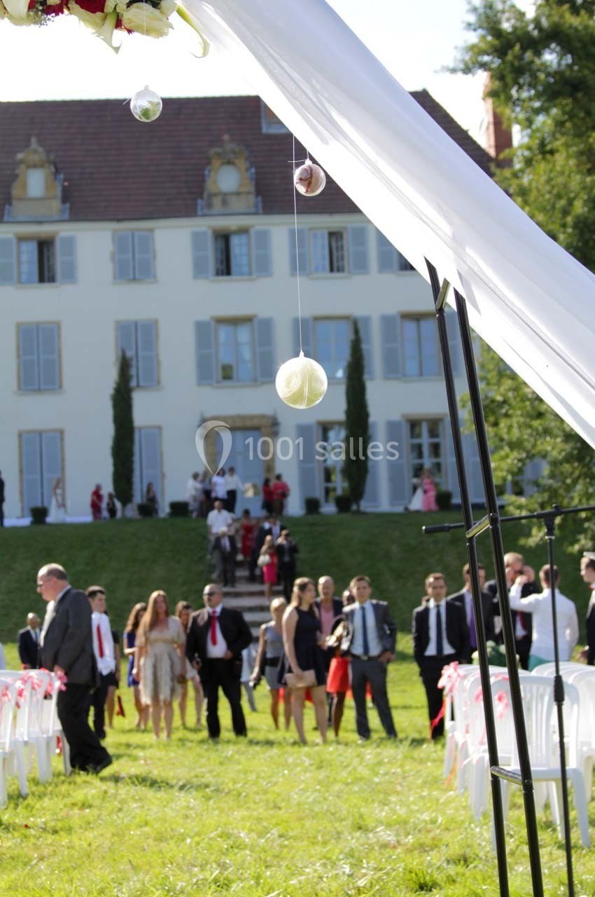 Cérémonie en plein air avec invités rassemblés devant un bâtiment historique, décorée de voilages et ornements suspendus.