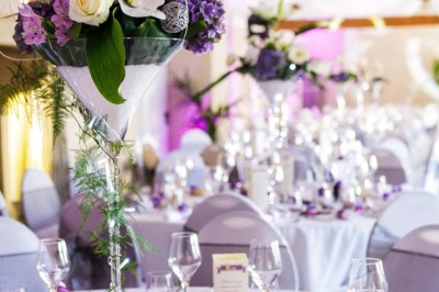 Allée gravillonnée bordée de lanternes blanches menant à un jardin arboré, vue depuis un portail en fer forgé.