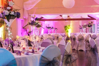 Allée gravillonnée bordée de lanternes blanches menant à un jardin arboré, vue depuis un portail en fer forgé.