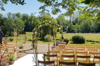 Allée gravillonnée bordée de lanternes blanches menant à un jardin arboré, vue depuis un portail en fer forgé.