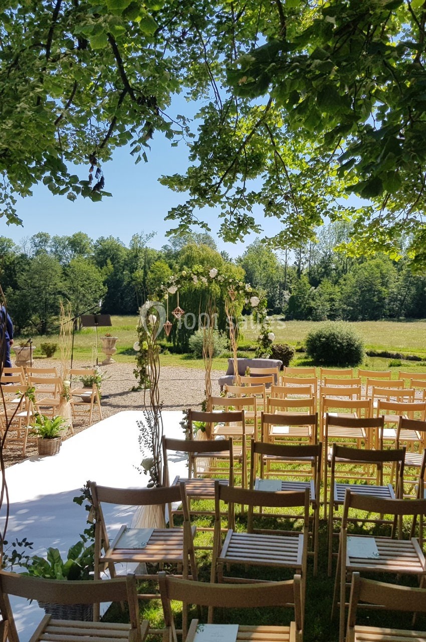Chaises en bois disposées en extérieur sous des arbres, face à une arche décorée pour une cérémonie champêtre.