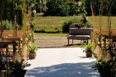 Allée gravillonnée bordée de lanternes blanches menant à un jardin arboré, vue depuis un portail en fer forgé.