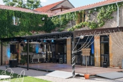Allée gravillonnée bordée de lanternes blanches menant à un jardin arboré, vue depuis un portail en fer forgé.