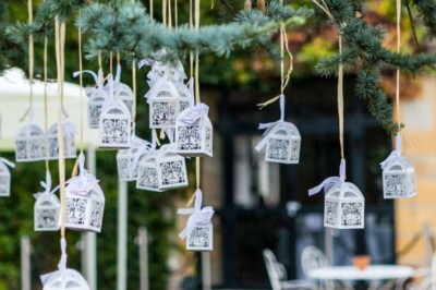 Allée gravillonnée bordée de lanternes blanches menant à un jardin arboré, vue depuis un portail en fer forgé.