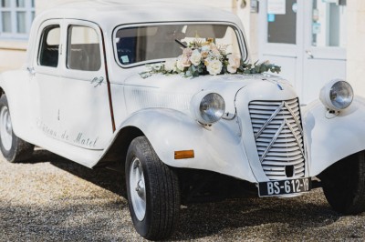 Allée gravillonnée bordée de lanternes blanches menant à un jardin arboré, vue depuis un portail en fer forgé.