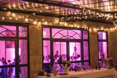 Allée gravillonnée bordée de lanternes blanches menant à un jardin arboré, vue depuis un portail en fer forgé.