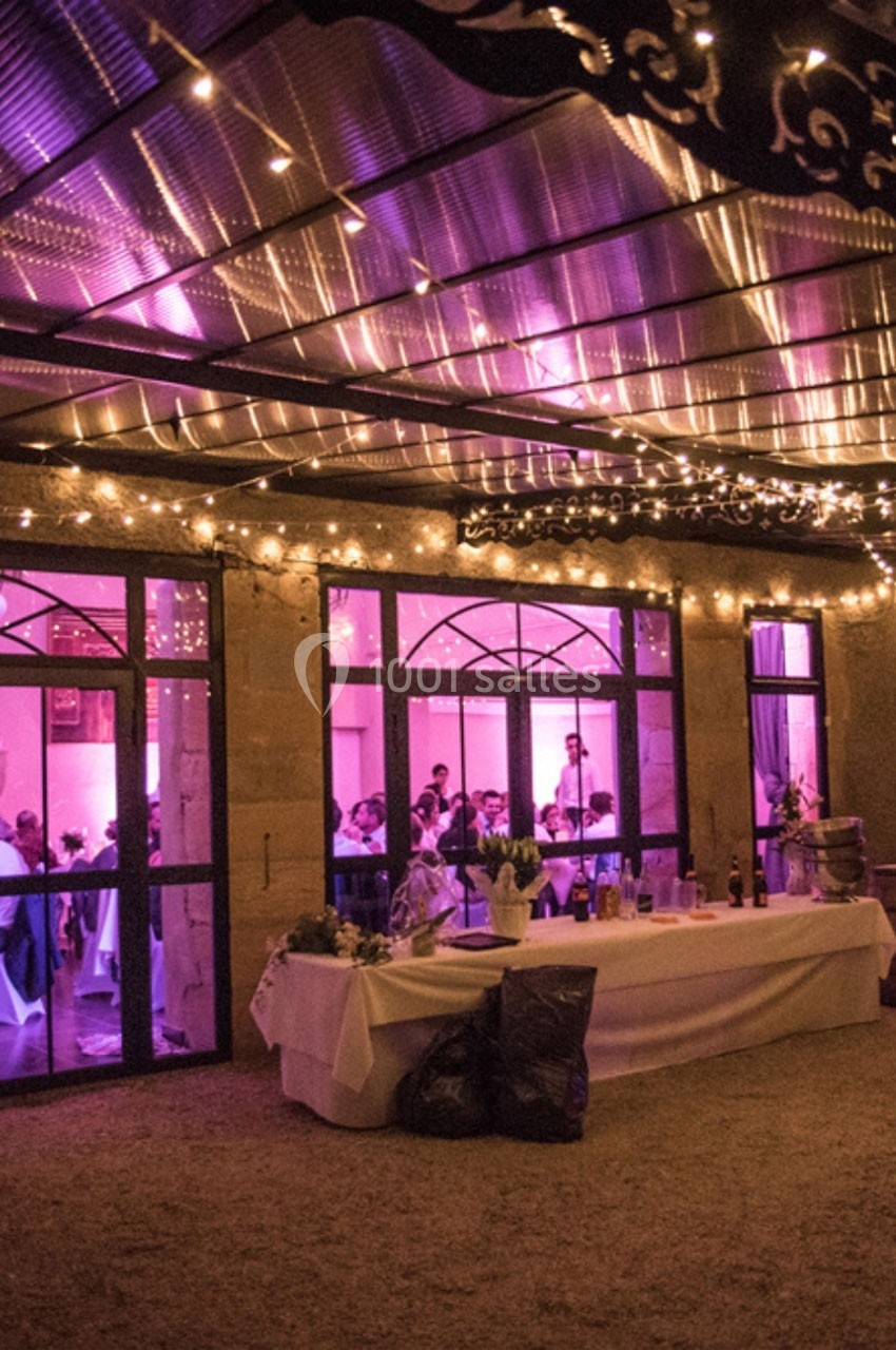 Salle de réception éclairée par des lumières violettes et guirlandes, avec des invités visibles à travers les fenêtres.