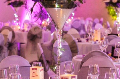 Allée gravillonnée bordée de lanternes blanches menant à un jardin arboré, vue depuis un portail en fer forgé.