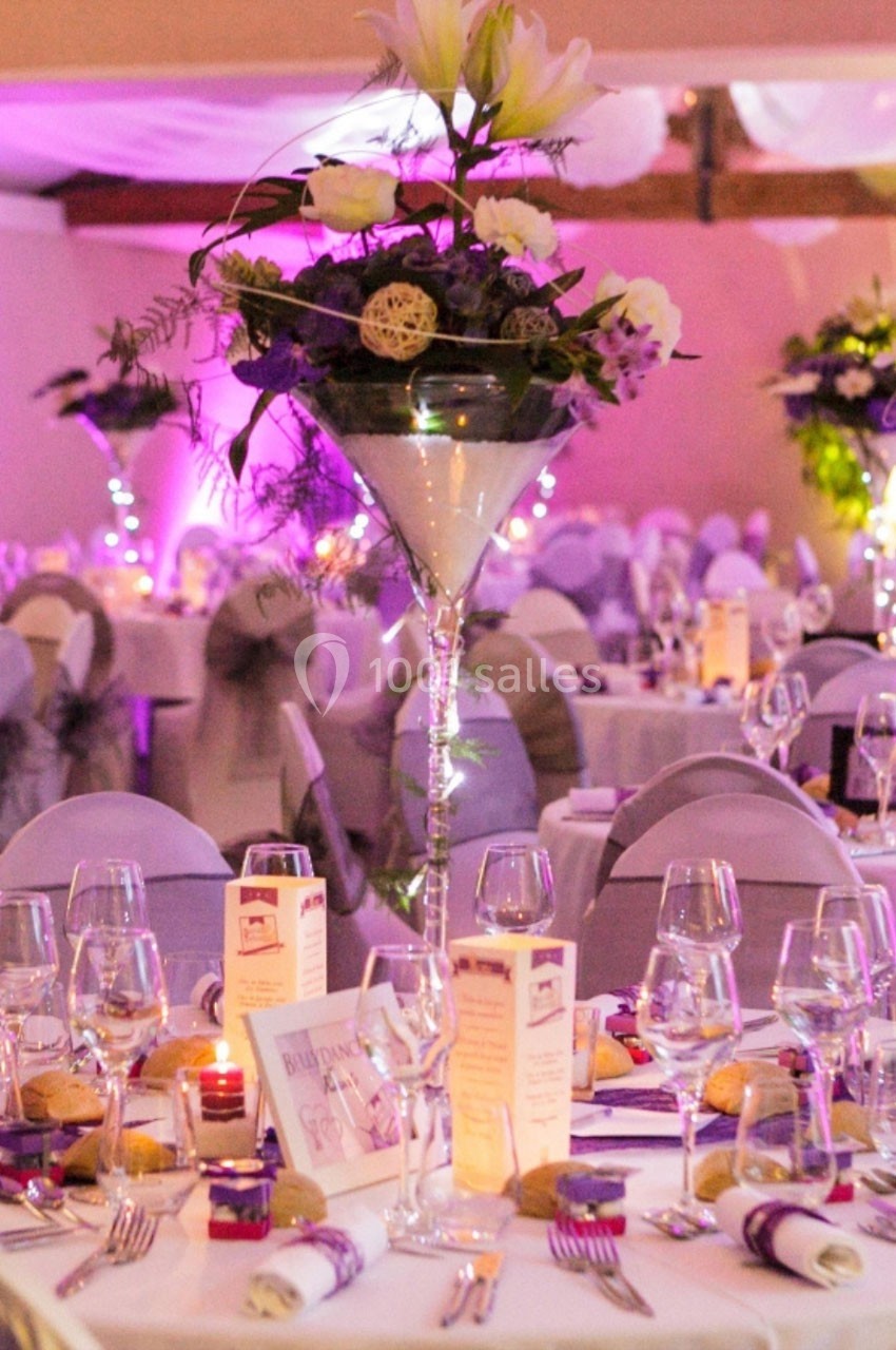 Salle de réception décorée avec des tables élégantes, des fleurs en centre de table et une ambiance lumineuse tamisée.