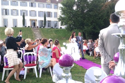 Allée gravillonnée bordée de lanternes blanches menant à un jardin arboré, vue depuis un portail en fer forgé.