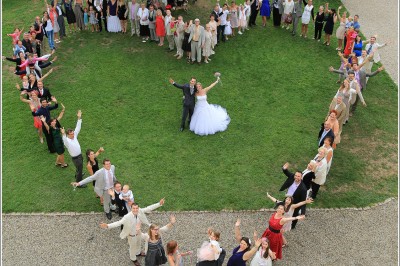 Allée gravillonnée bordée de lanternes blanches menant à un jardin arboré, vue depuis un portail en fer forgé.