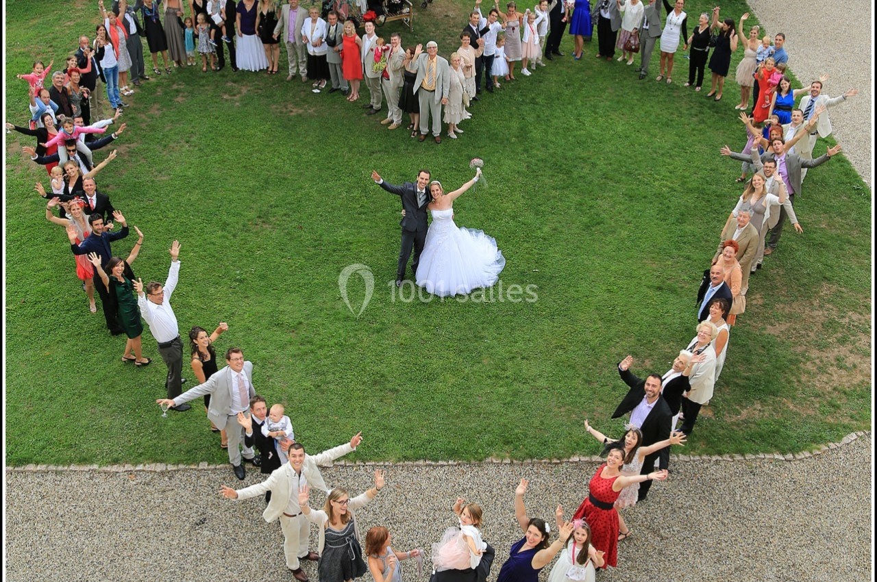 Groupe de personnes formant un cœur autour d'un couple de mariés sur une pelouse, vu en plongée.
