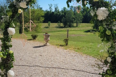 Allée gravillonnée bordée de lanternes blanches menant à un jardin arboré, vue depuis un portail en fer forgé.