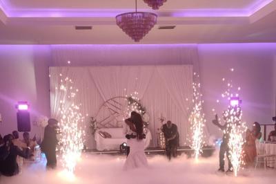 Salle de réception élégante avec un arc floral blanc, des tables décorées et un éclairage lumineux.