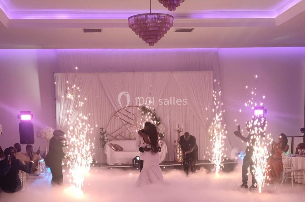 Un couple danse au centre d'une salle décorée, entouré d'effets pyrotechniques et d'un sol couvert de fumée.