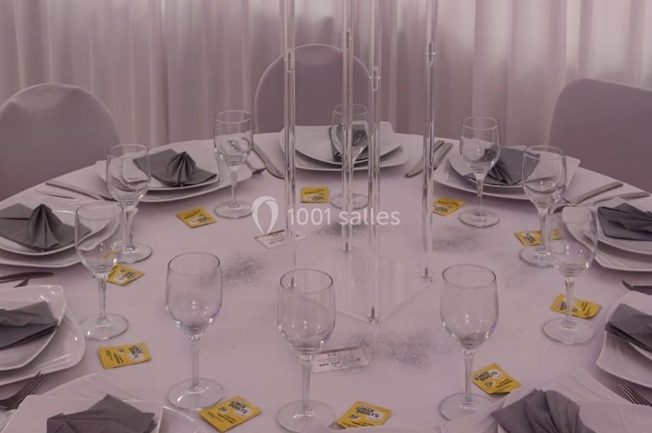 Table ronde dressée avec nappes blanches, serviettes grises pliées, verres à vin et décorations minimalistes.