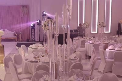 Salle de réception élégante avec un arc floral blanc, des tables décorées et un éclairage lumineux.