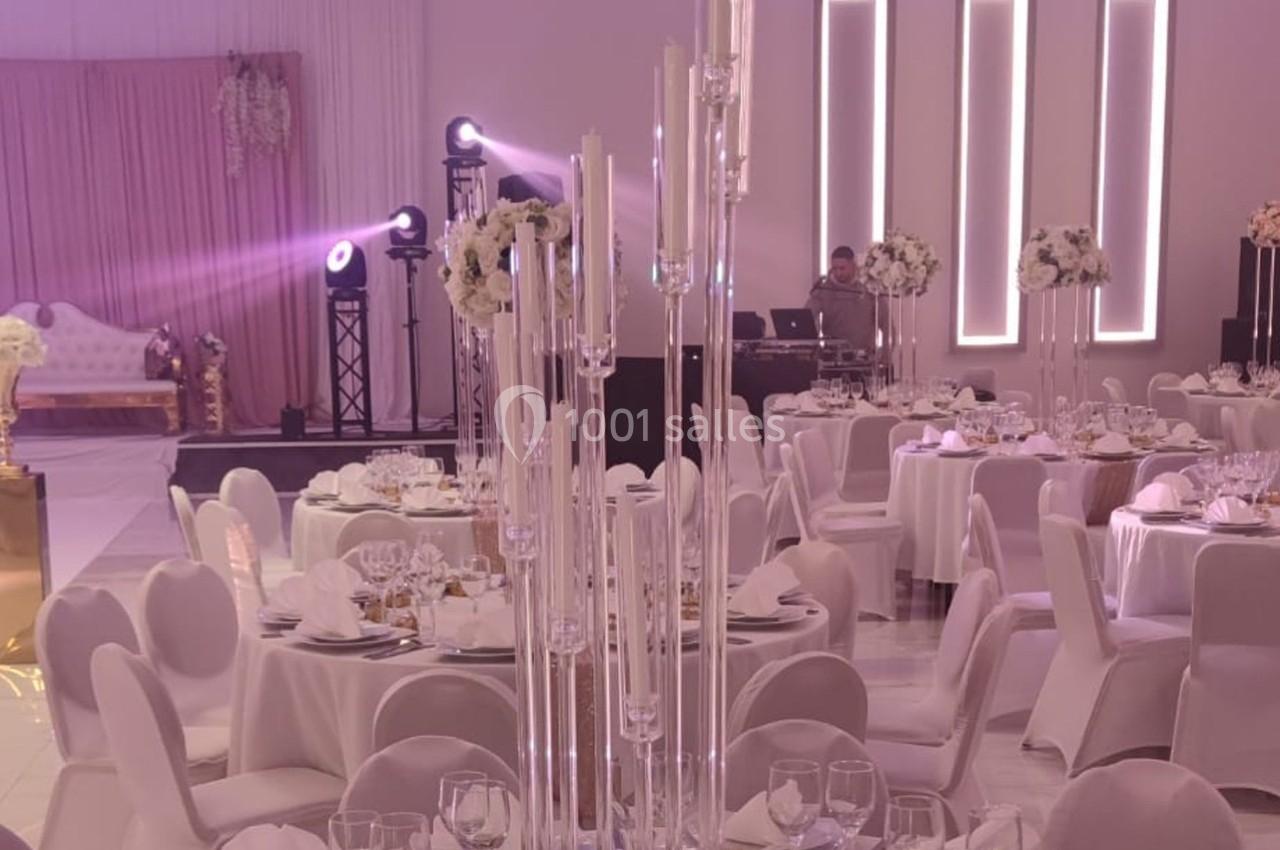 Salle de réception élégante avec tables dressées, chandeliers en verre et éclairage d'ambiance moderne.
