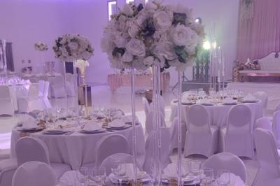 Salle de réception élégante avec un arc floral blanc, des tables décorées et un éclairage lumineux.