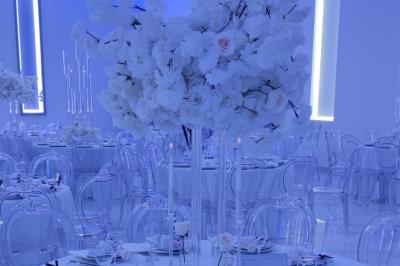 Salle de réception élégante avec un arc floral blanc, des tables décorées et un éclairage lumineux.