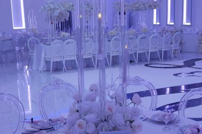 Salle de réception élégante avec un arc floral blanc, des tables décorées et un éclairage lumineux.