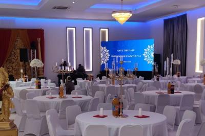 Salle de réception élégante avec un arc floral blanc, des tables décorées et un éclairage lumineux.