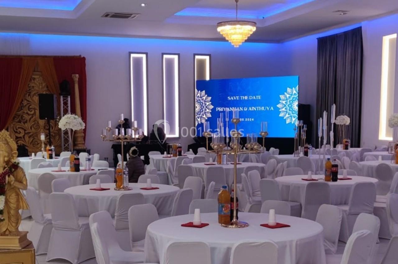 Salle de réception décorée avec des tables rondes, chaises blanches et un écran affichant un message de réservation.