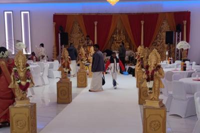 Salle de réception élégante avec un arc floral blanc, des tables décorées et un éclairage lumineux.