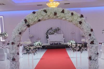 Salle de réception élégante avec un arc floral blanc, des tables décorées et un éclairage lumineux.