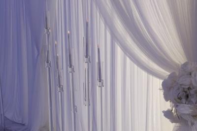 Salle de réception élégante avec un arc floral blanc, des tables décorées et un éclairage lumineux.
