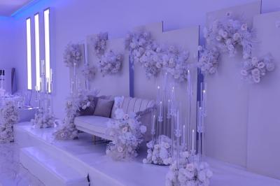 Salle de réception élégante avec un arc floral blanc, des tables décorées et un éclairage lumineux.